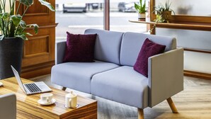 A modern living room with a grey sofa, two purple cushions, a wooden coffee table with a laptop, two white cups, and a potted plant. - Novotel Bristol Centre (Bristol)