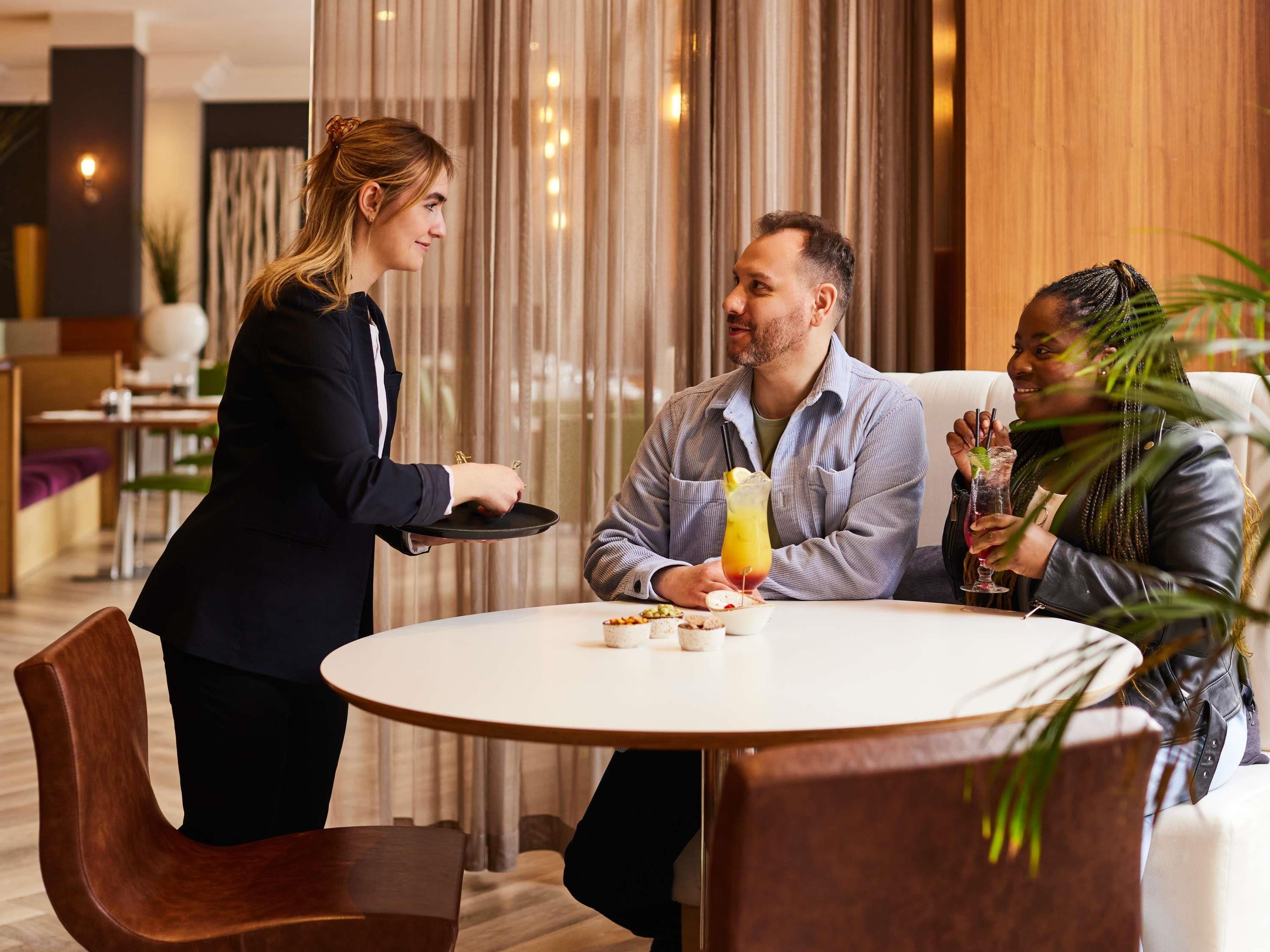 A hotel dining area with a round table, chairs, and a waiter serving food.
