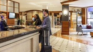 A hotel reception area with a marble counter, a television, and a seating area with a sofa and armchairs. - Novotel Bristol Centre (Bristol)