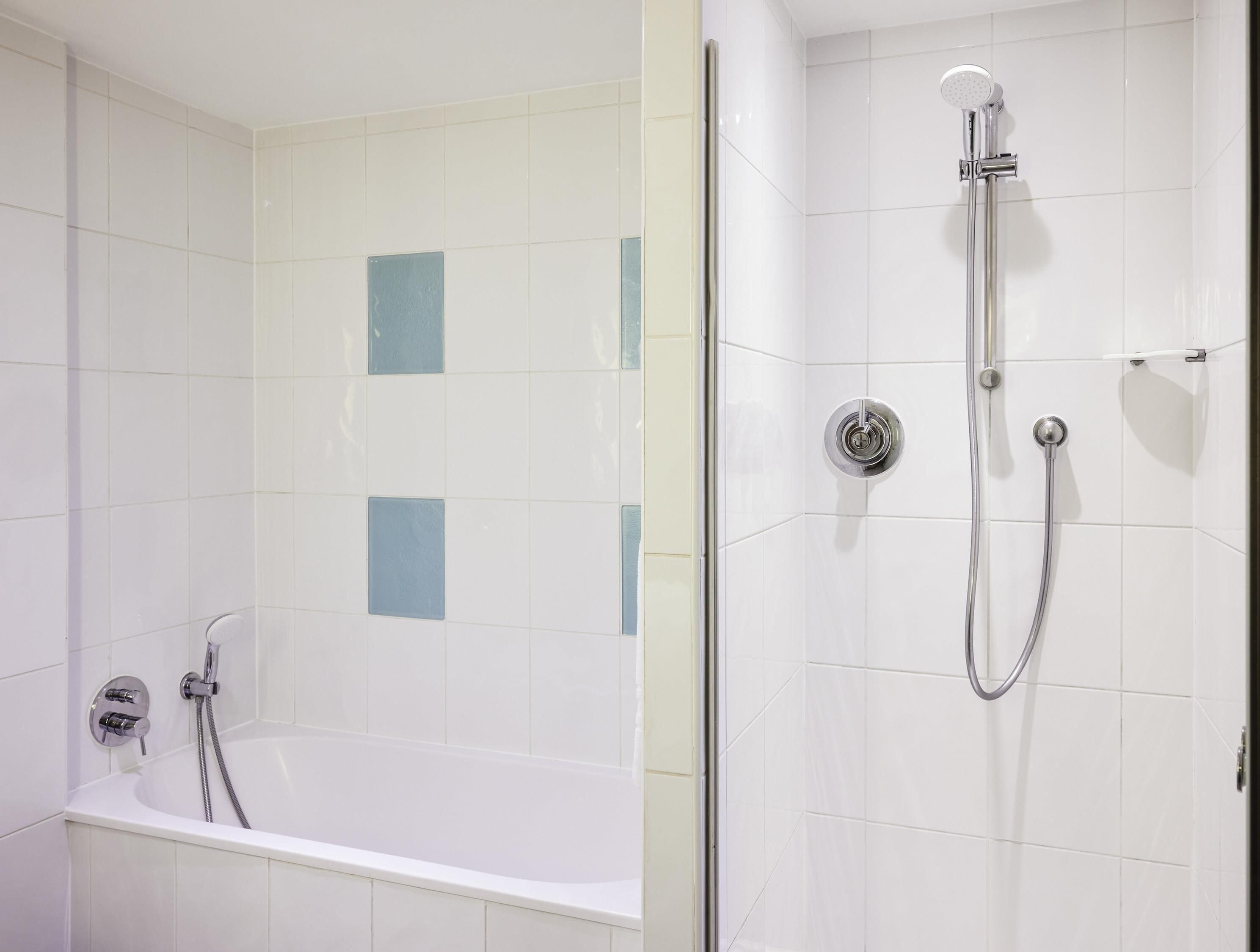 Une salle de bain dotée d’une baignoire et d’un espace douche, les deux étant caractérisés par des murs recouverts de carreaux blancs et un design moderne.