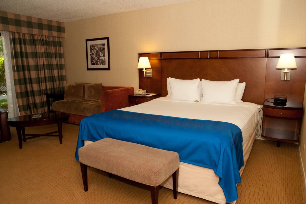 A hotel room with a large bed, a bench, a chair, a desk, and two bedside lamps.