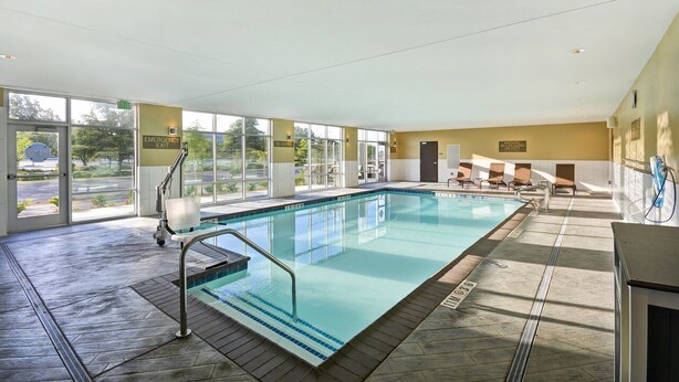 An indoor swimming pool with clear glass walls, a pool ladder, and a few lounge chairs.