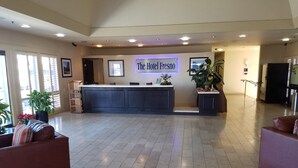A hotel lobby with a reception desk, a large potted plant, and a sign reading "The Hotel Fresno".