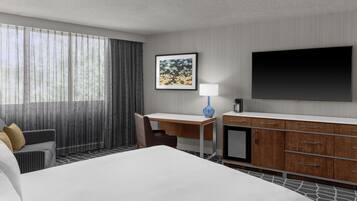 Ett hotellrum med en säng, ett skrivbord, en stol, en tv och ett fönster med gardiner.