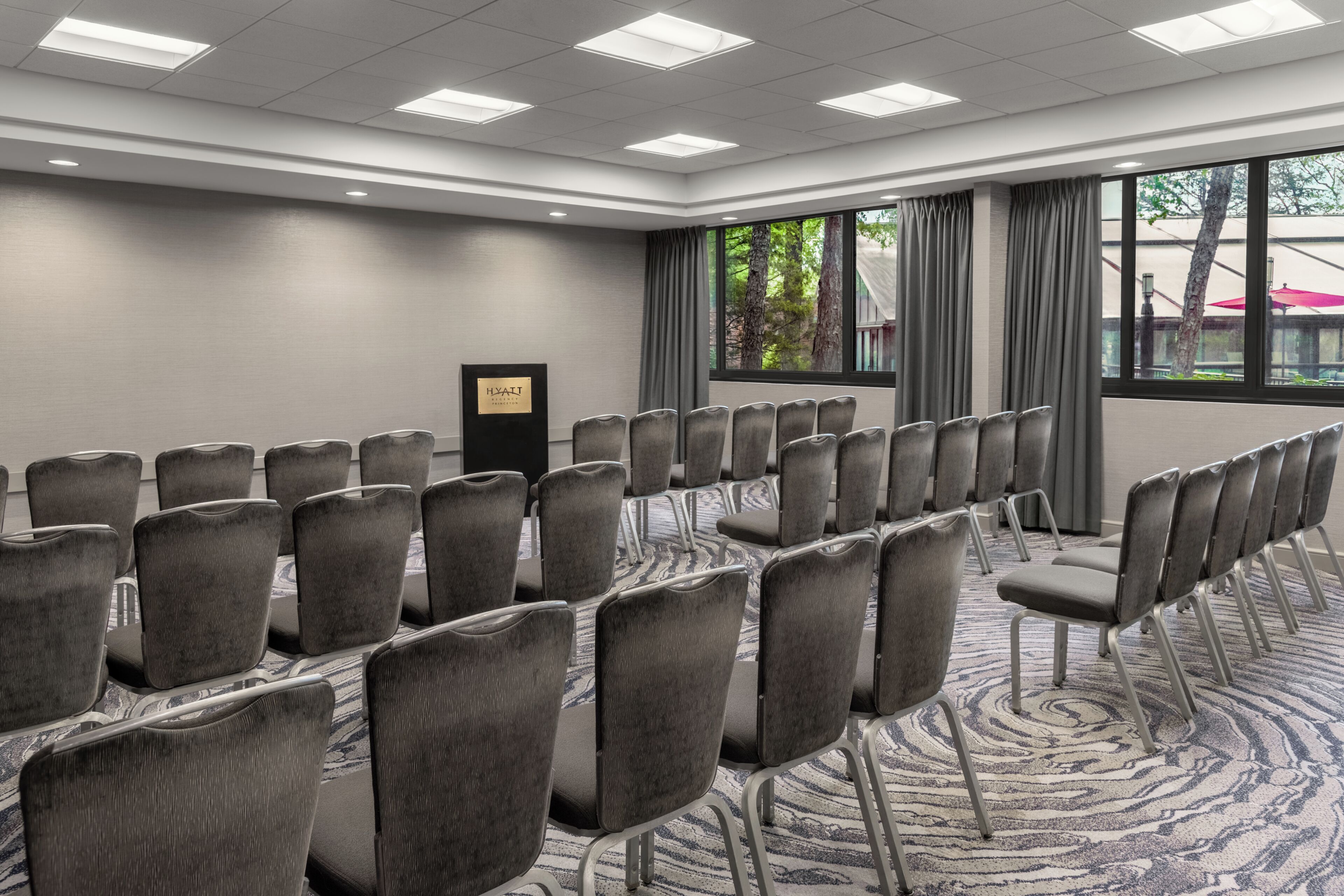 A conference room with rows of chairs, a podium, and a large window with curtains.