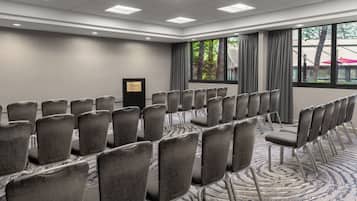Un salón de conferencias con filas de sillas, un atril y un amplio ventanal con cortinas.