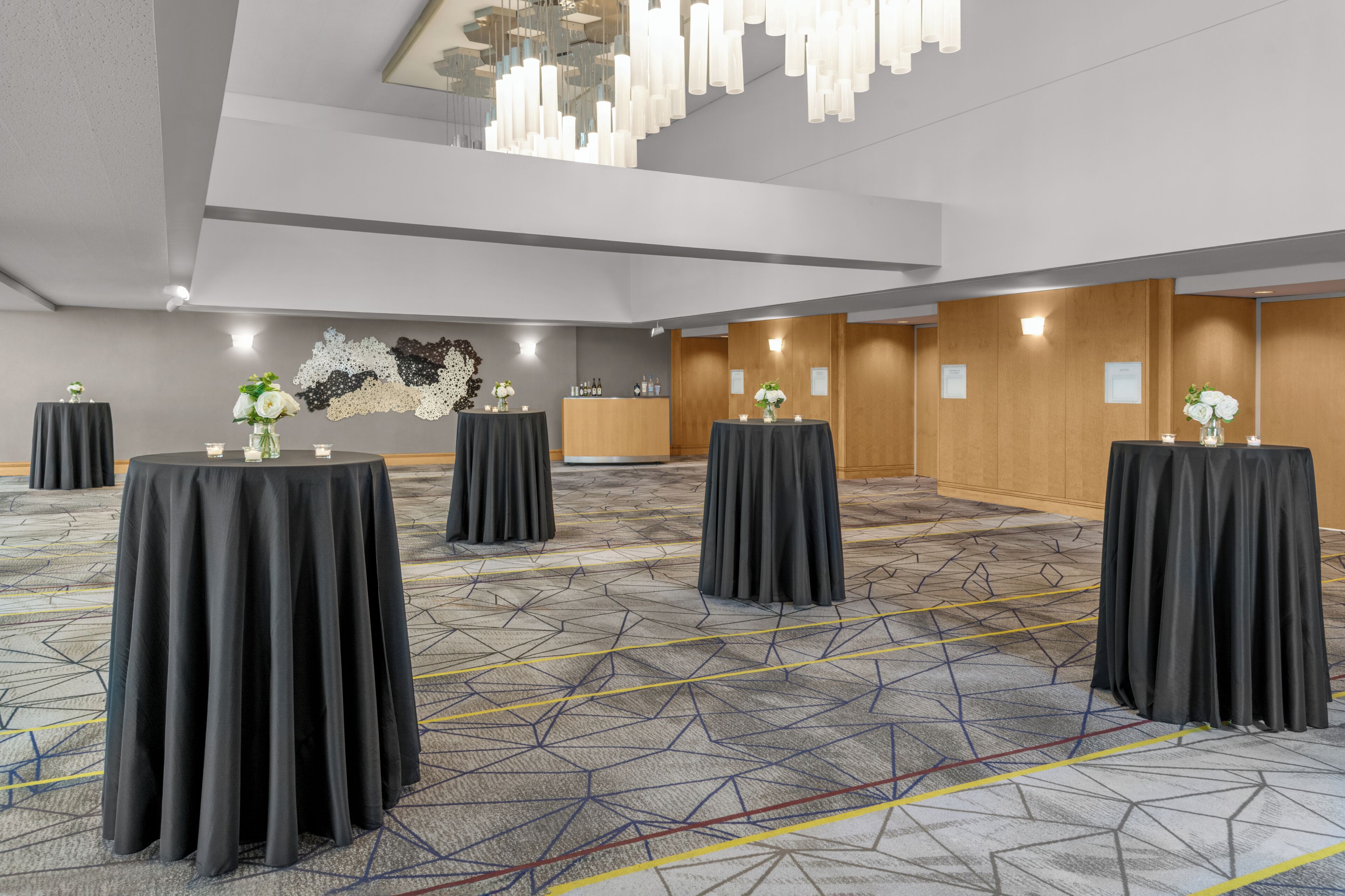 A conference room with multiple tables, a geometric patterned carpet, and a modern chandelier.