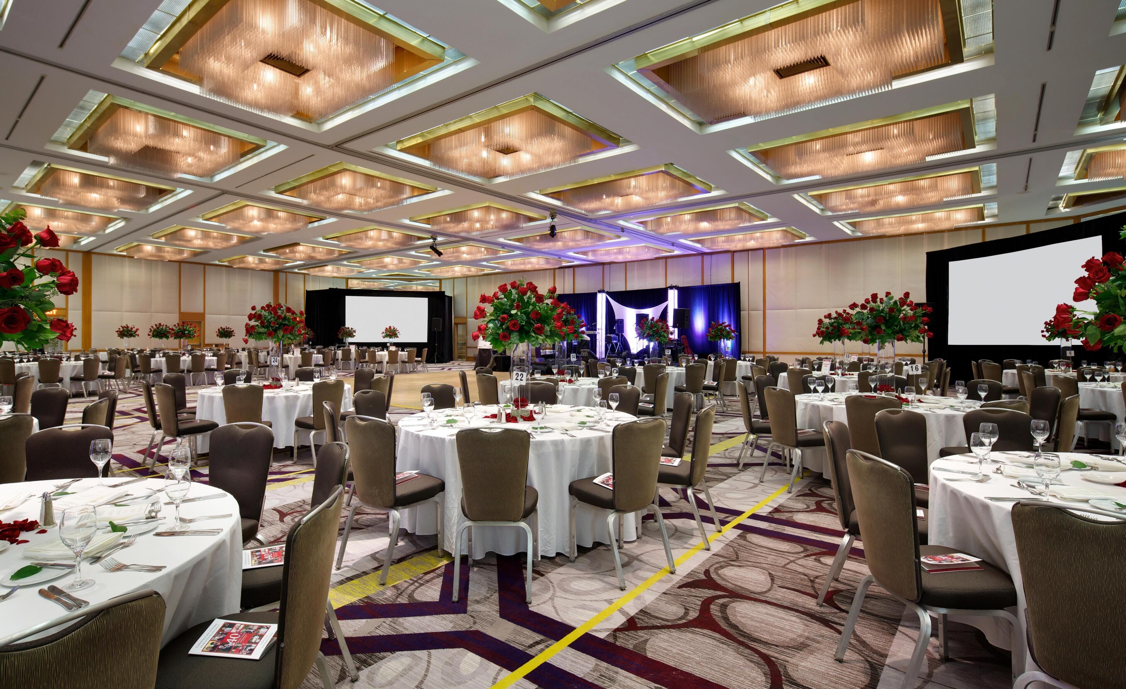 A large banquet hall with round tables, chairs, and floral centerpieces.