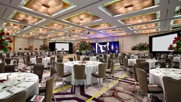 A large banquet hall with round tables, chairs, and floral centerpieces.