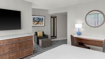 A hotel room with a bed, a desk, a chair, a TV, a framed picture, a mirror, and a lamp.