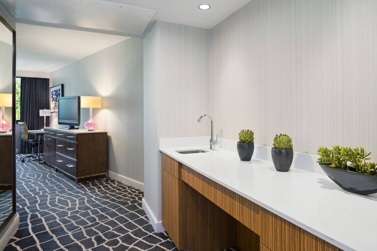 A modern hotel bathroom with a white countertop, a sink, and potted plants.