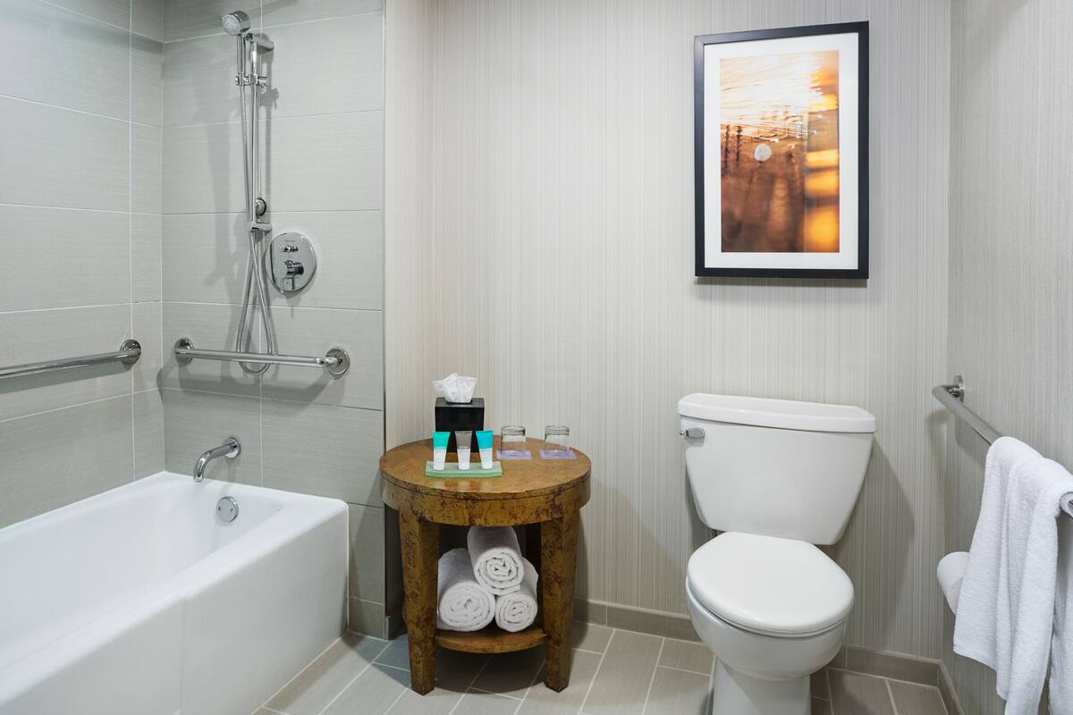A bathroom with a bathtub, toilet, and a small wooden stool with toiletries.