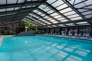 An indoor swimming pool with a glass ceiling, surrounded by lounge chairs and a small garden area. - Hyatt Regency Princeton (Princeton)