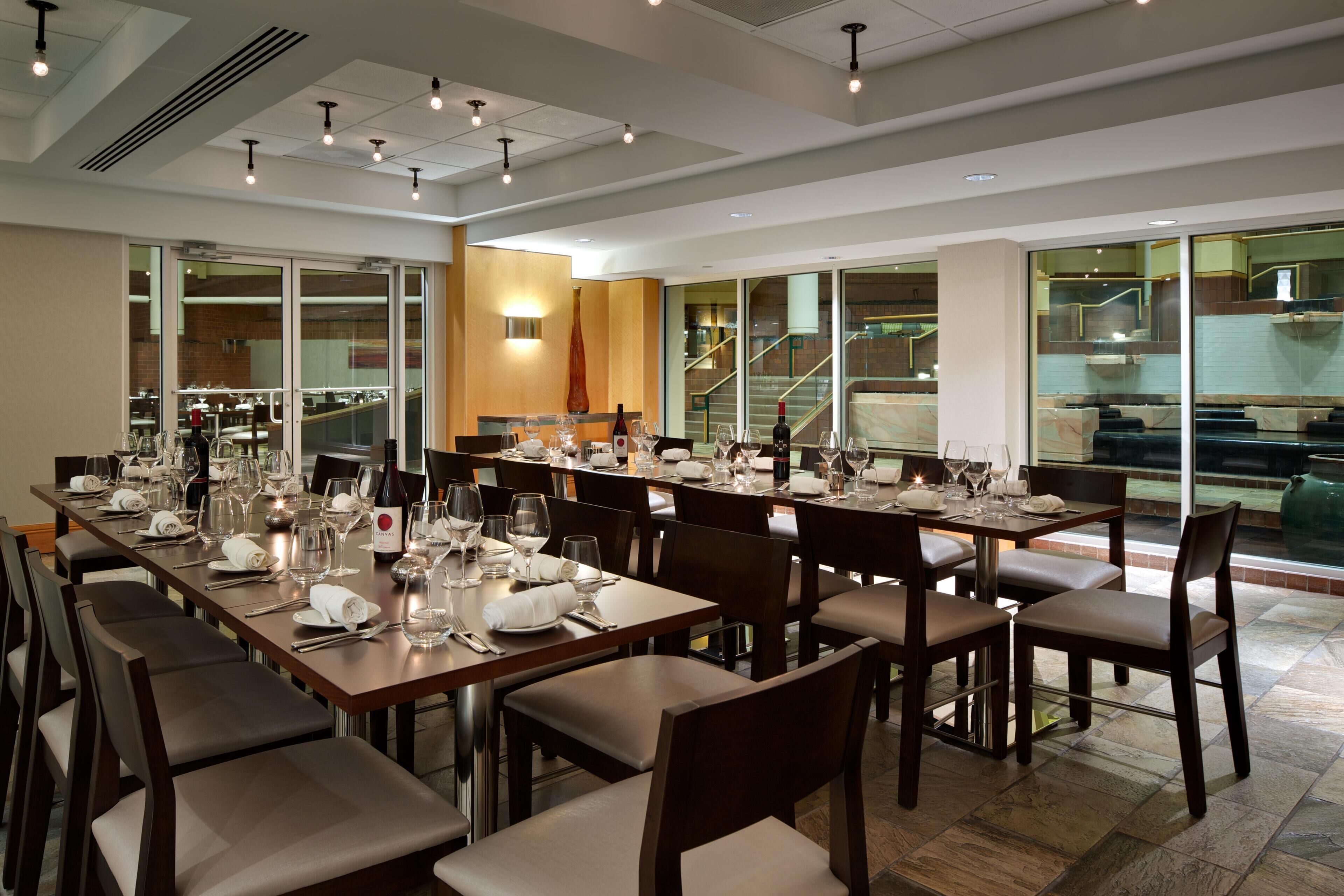 A spacious dining area with multiple tables set for a meal, large windows offering views of the interior, and a modern ceiling design with recessed lighting.