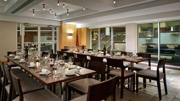 A spacious dining area with multiple tables set for a meal, large windows offering views of the interior, and a modern ceiling design with recessed lighting.