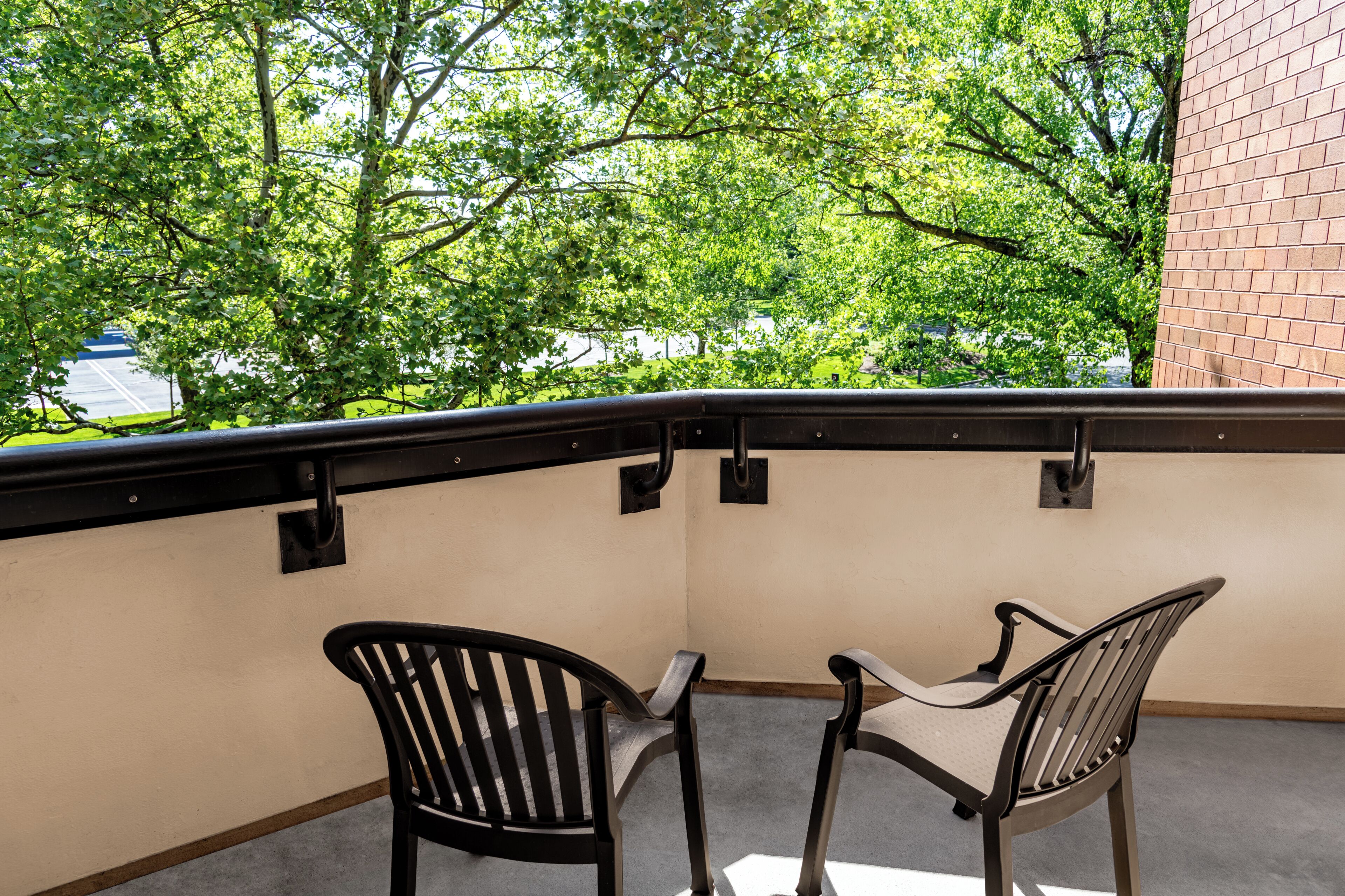 A balcony with two chairs, a brick wall, and trees in the background.