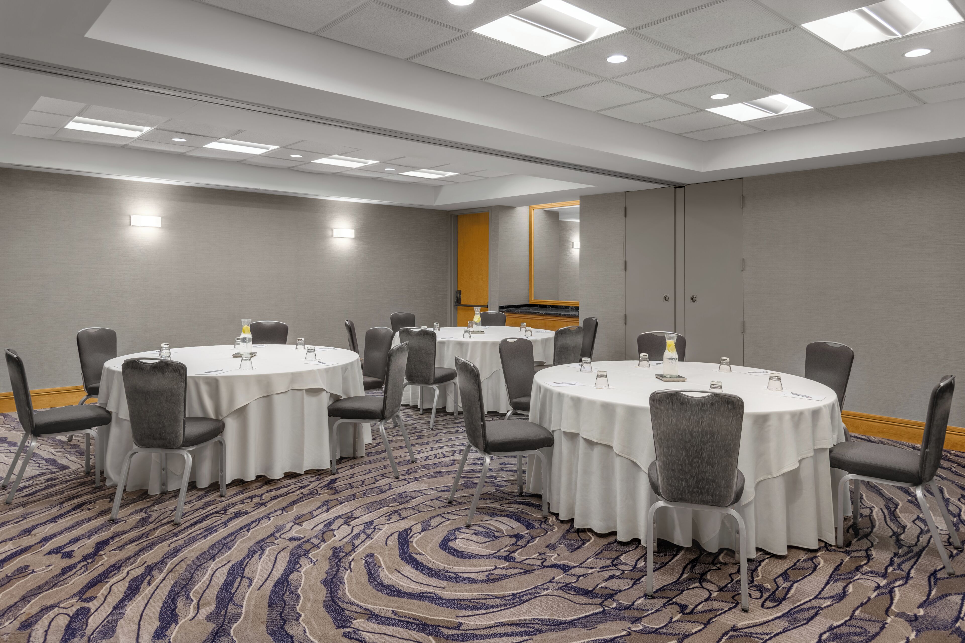 A conference room with round tables, chairs, and a carpeted floor.