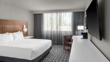 Habitación de hotel con cama, escritorio, silla, televisor y ventana con cortinas.