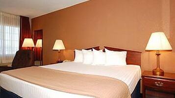 A hotel room with a large bed, two bedside lamps, a wooden headboard, and a window with curtains.