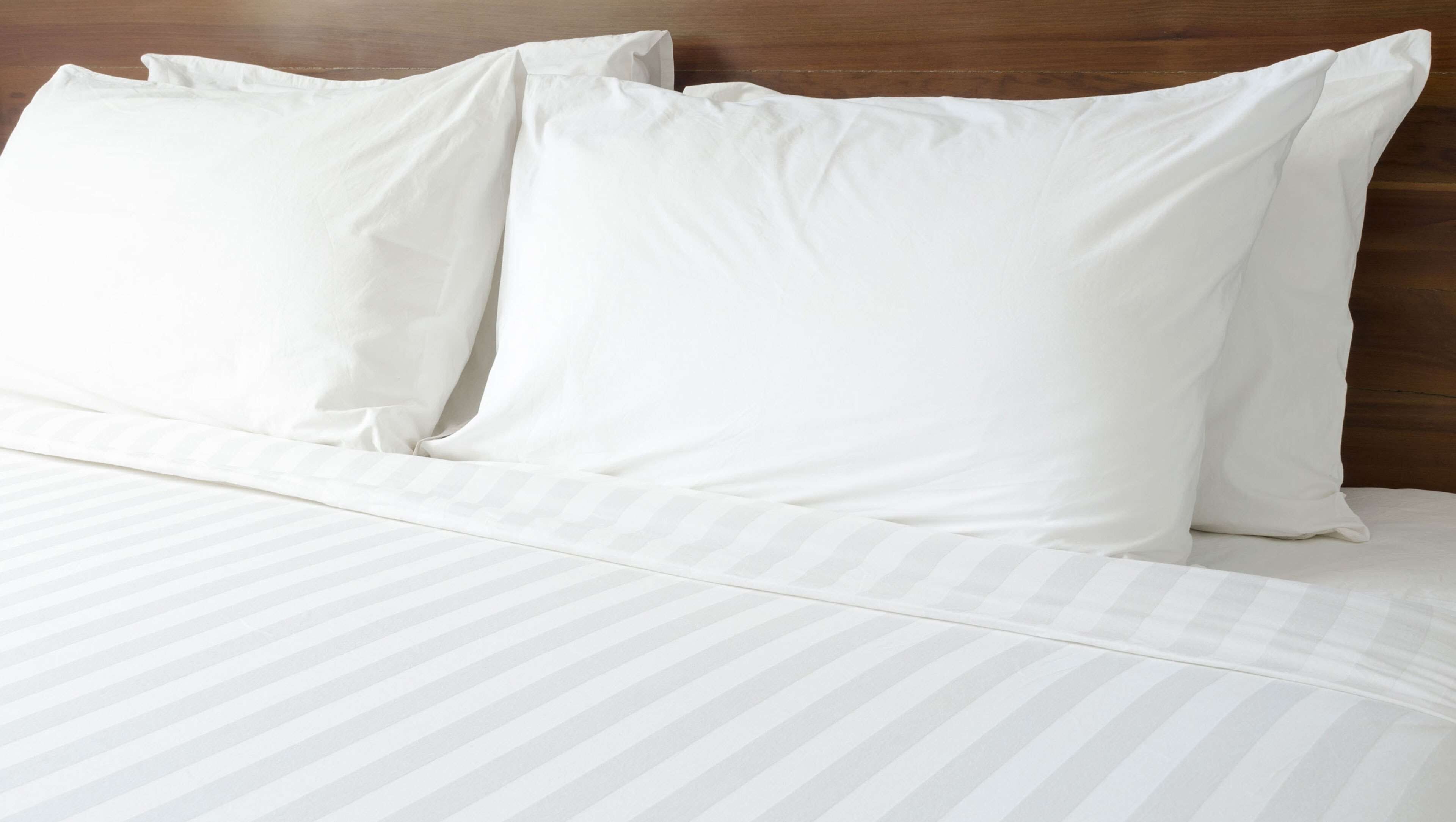 A neatly made bed with white bedding and striped sheets.