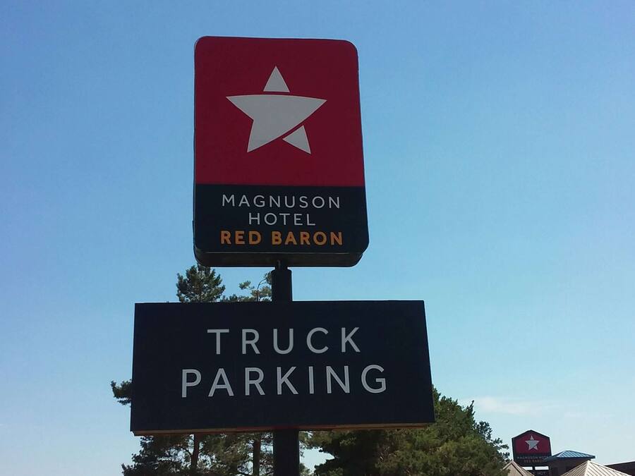 Señal del Hotel Magnuson Red Baron con un letrero de estacionamiento para camiones debajo.