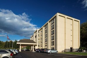 A multi-story hotel with a parking lot, a covered entrance, and a flag.