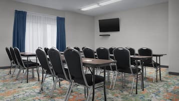 A conference room with a large table, multiple chairs, a flat-screen TV, and a patterned carpet.
