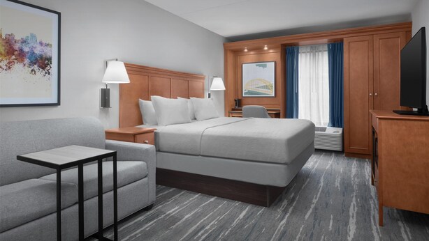 A hotel room with a bed, a sofa, a small table, a TV, a lamp, and a painting on the wall. - Hampton Inn Pittsburgh/Greentree (Pittsburgh)