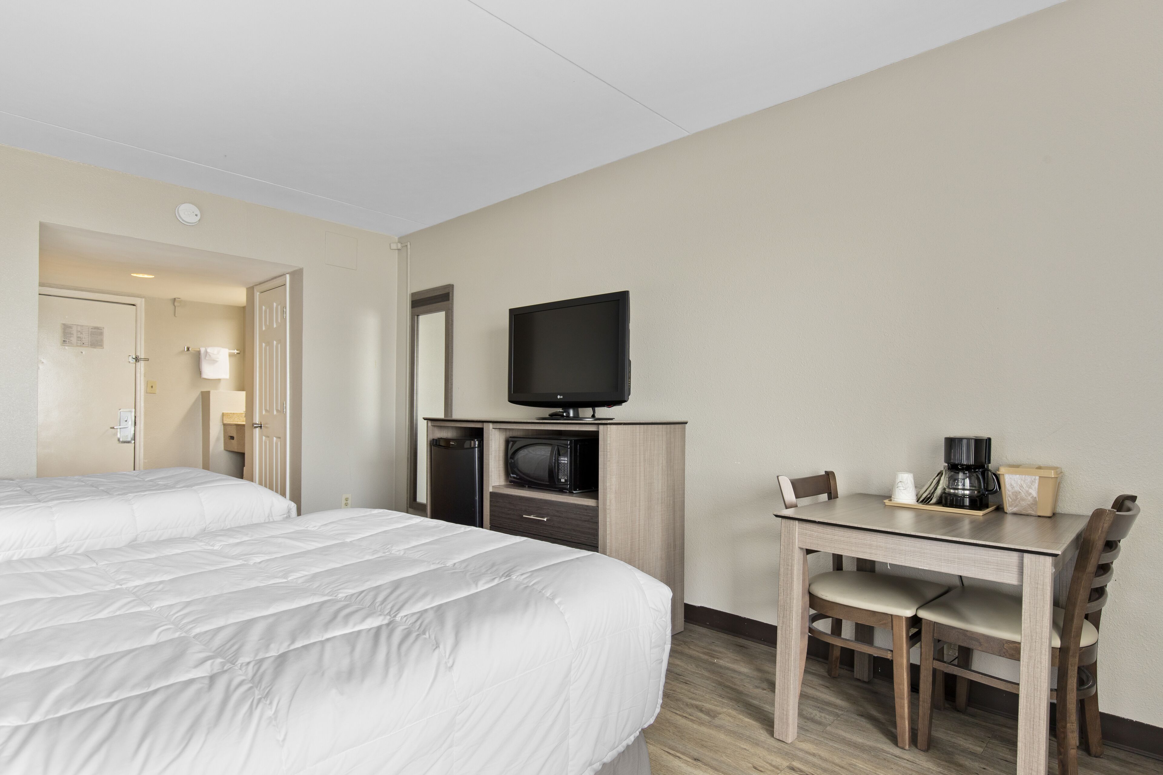 A hotel room with two beds, a desk with a chair, a television, a microwave, and a coffee maker.