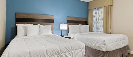 A hotel room with two beds, a nightstand, and a lamp.
