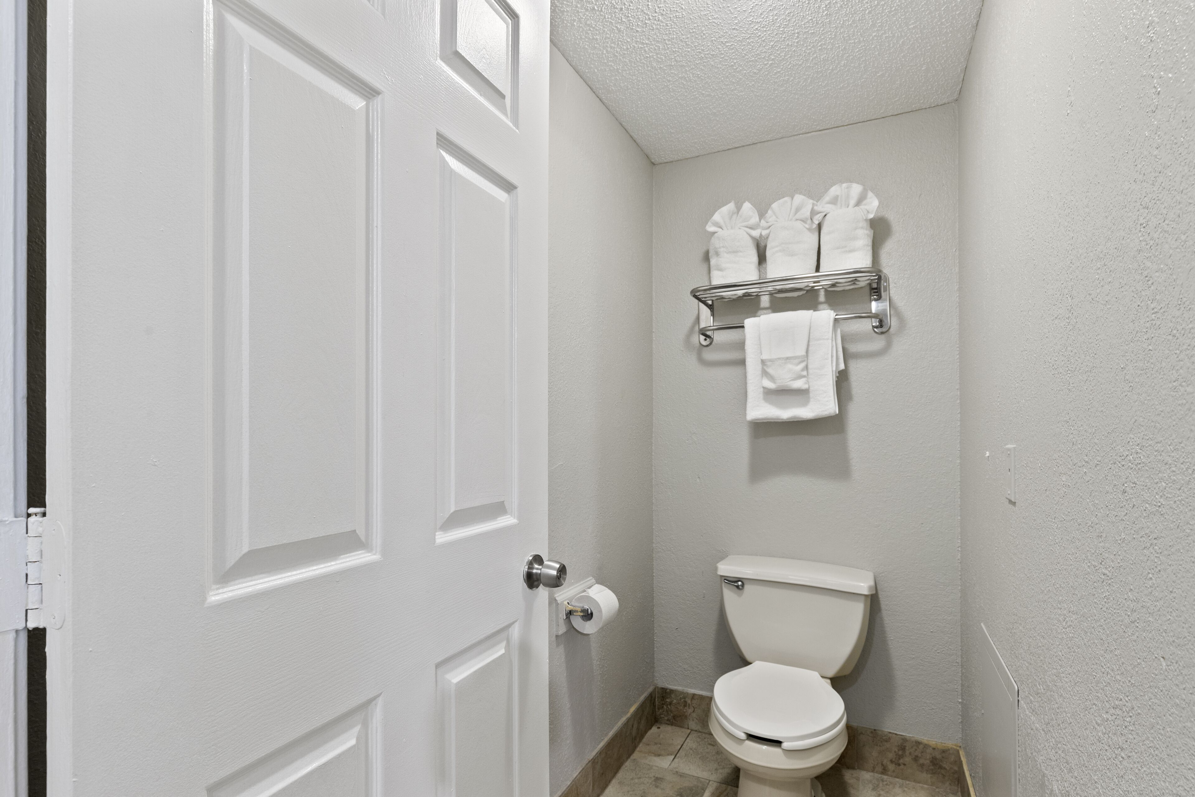 A bathroom with a white toilet, a towel rack with towels, and a door with a handle.