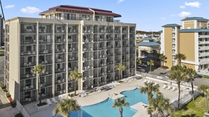 A multi-story hotel with balconies, a swimming pool, and palm trees. - Atlantic crest inn and suites (Myrtle Beach)