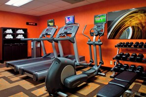 A gym with treadmills, an elliptical, a bench, and a wall-mounted TV. - Courtyard Syracuse Carrier Circle (East Syracuse)