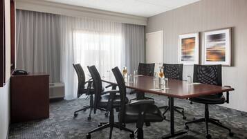 A conference room with a long table, four chairs, a podium, and two framed abstract paintings on the wall.