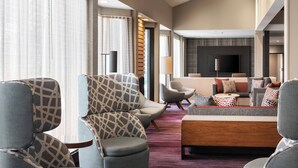 Un moderno vestíbulo de hotel con un área de estar que incluye sofás y sillones, un televisor de pantalla plana y una mesa de centro de madera.