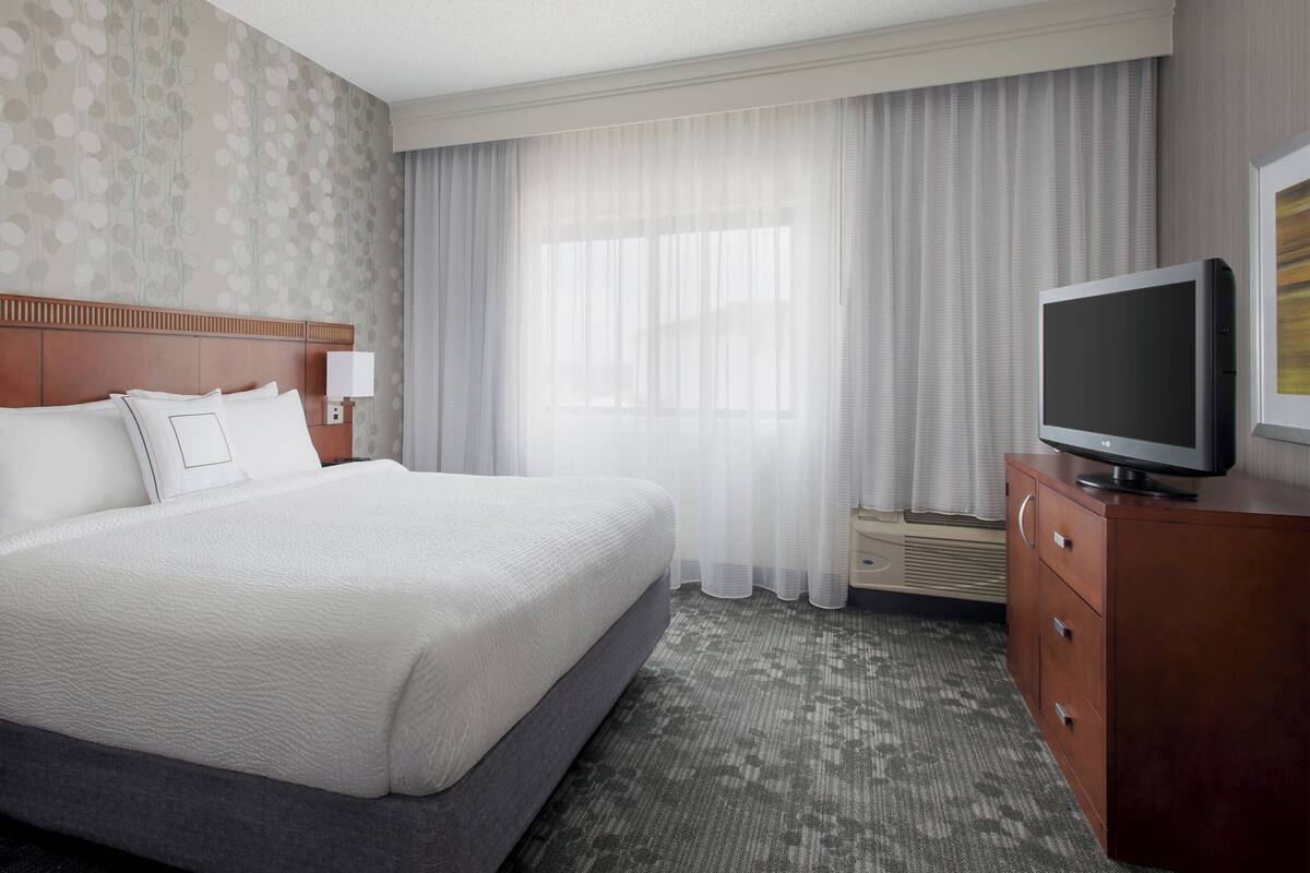 A hotel room with a large bed, a TV, a dresser, and a window with curtains.