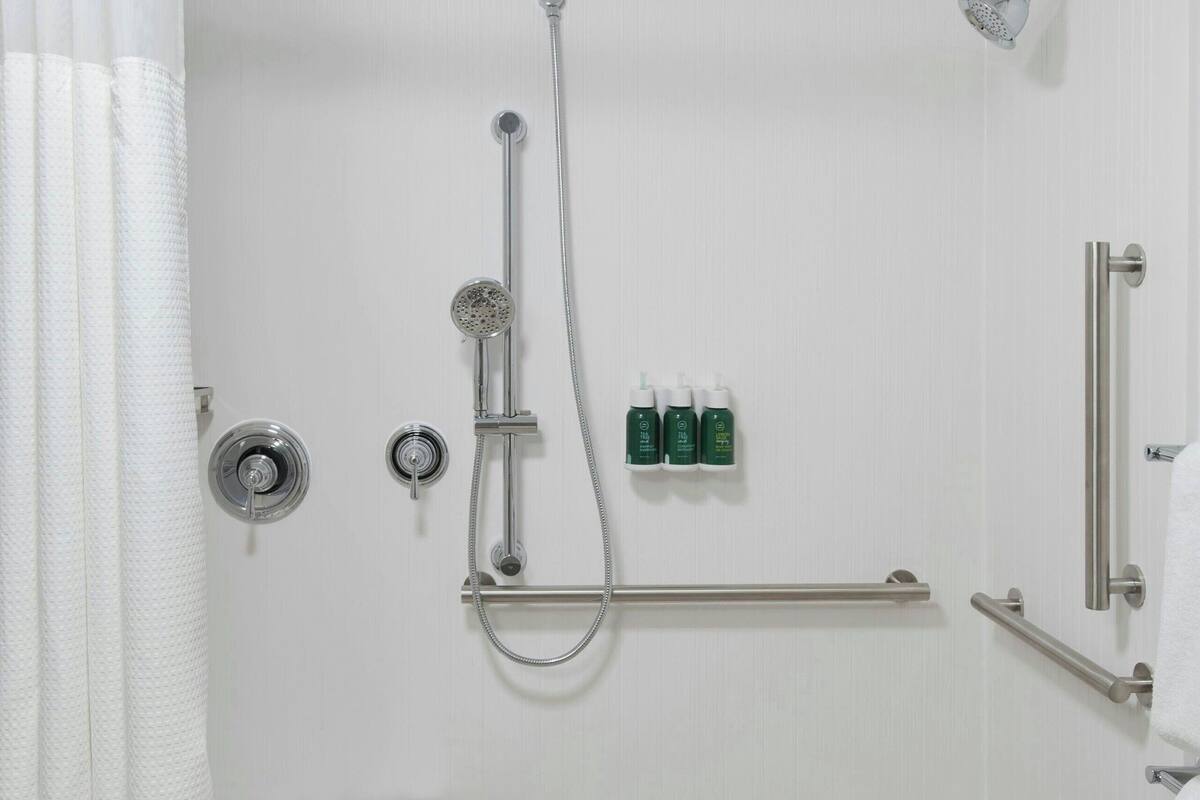 A modern bathroom with a shower, grab bars, and a bench.