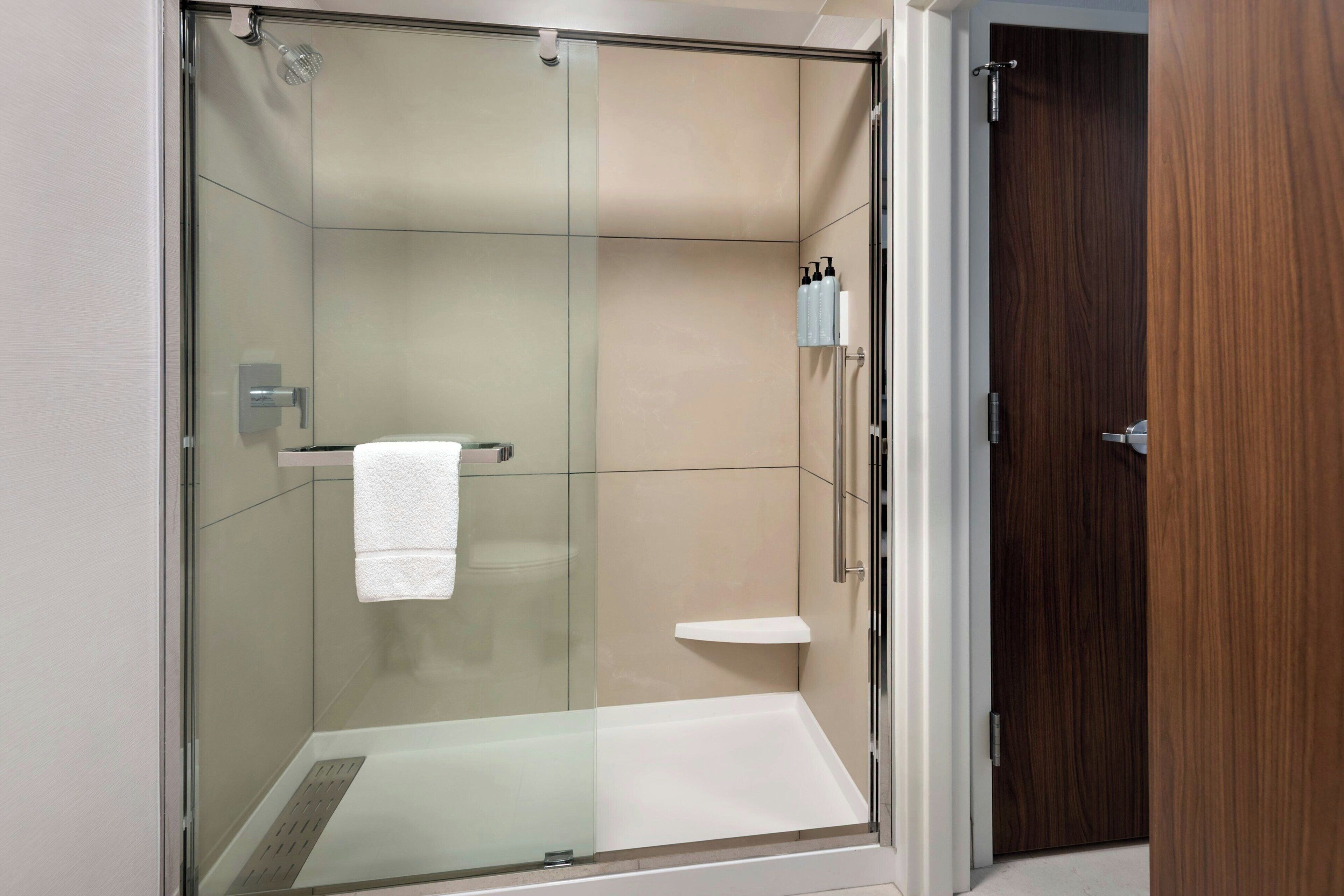 A modern bathroom with a glass-enclosed shower, a white towel hanging on a rack, and a wooden door.