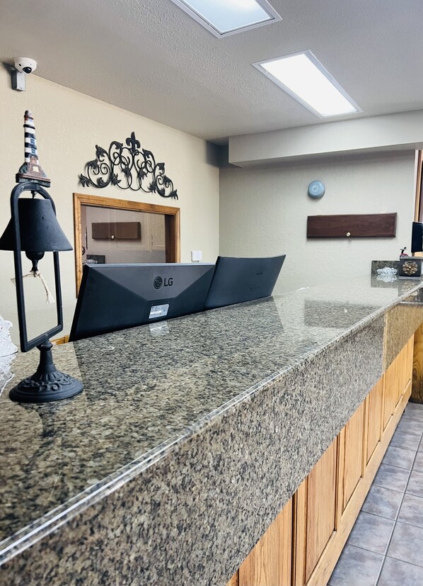 A reception desk with an LG monitor, a security camera, a decorative wall piece, and a clock.
