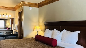 A hotel room with a large bed, a wooden headboard, a bedside table, a lamp, a mirror, and a dresser. - Cattle Country Lodge (Stroud)