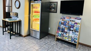 A room with a refrigerator stocked with beverages, a clock, a television, and a display of travel brochures. - Cattle Country Lodge (Stroud)