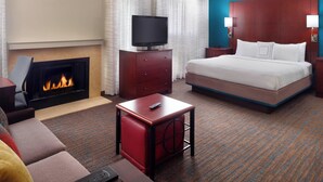 Habitación de hotel con chimenea, cama, televisor sobre un mueble de madera, una mesita auxiliar roja y una pared de acento azul.