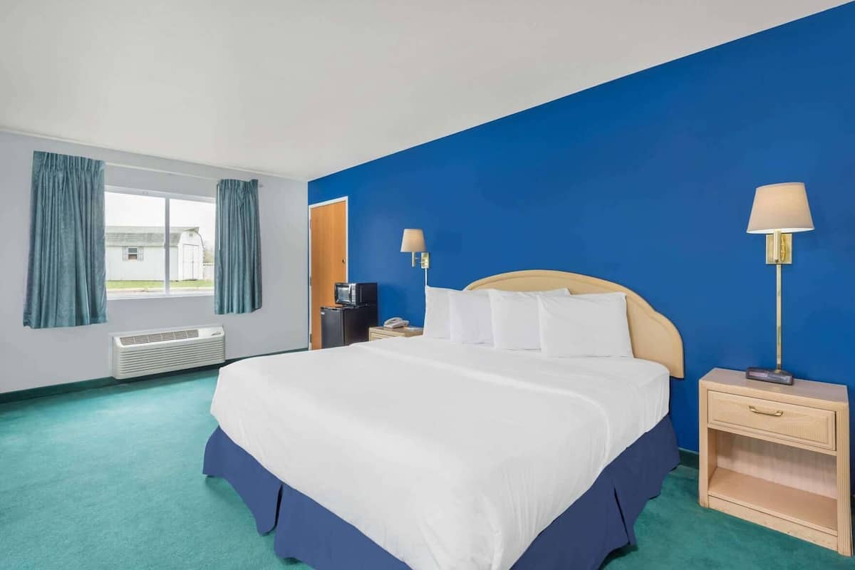 Ein Hotelzimmer mit einem großen Bett, zwei Nachttischlampen, einer Heizung und einem Fenster mit Vorhängen.