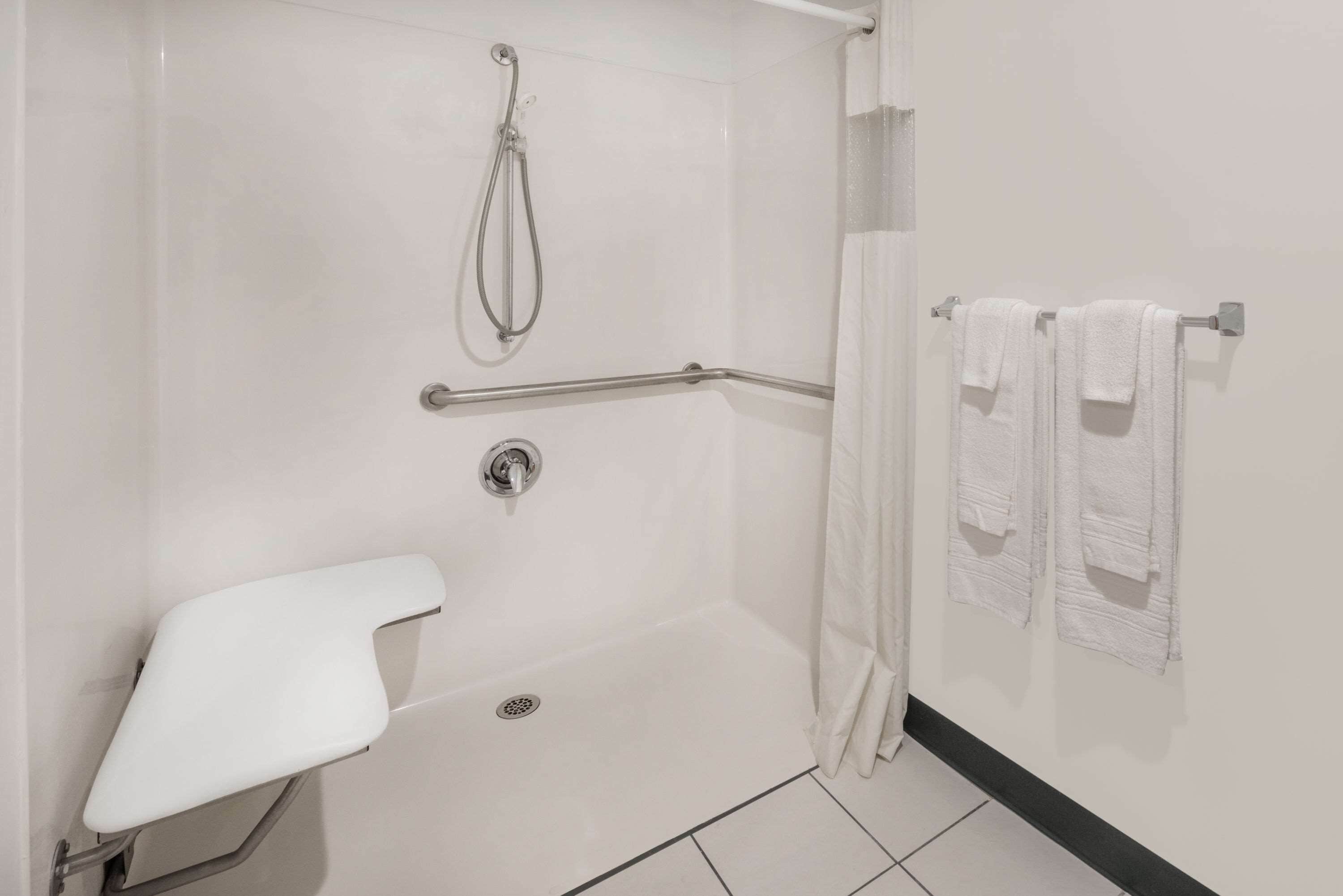 A modern bathroom with a walk-in shower, grab bars, a white toilet, and towels on a rack.