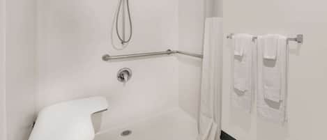 A modern bathroom with a walk-in shower, grab bars, a white toilet, and towels on a rack.