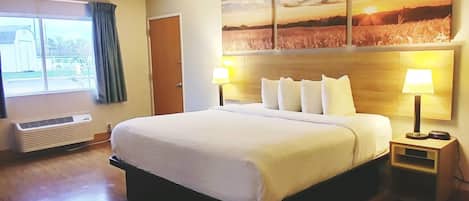 A hotel room with a large bed, a bedside table with a lamp, a wall-mounted air conditioner, and a window with curtains.