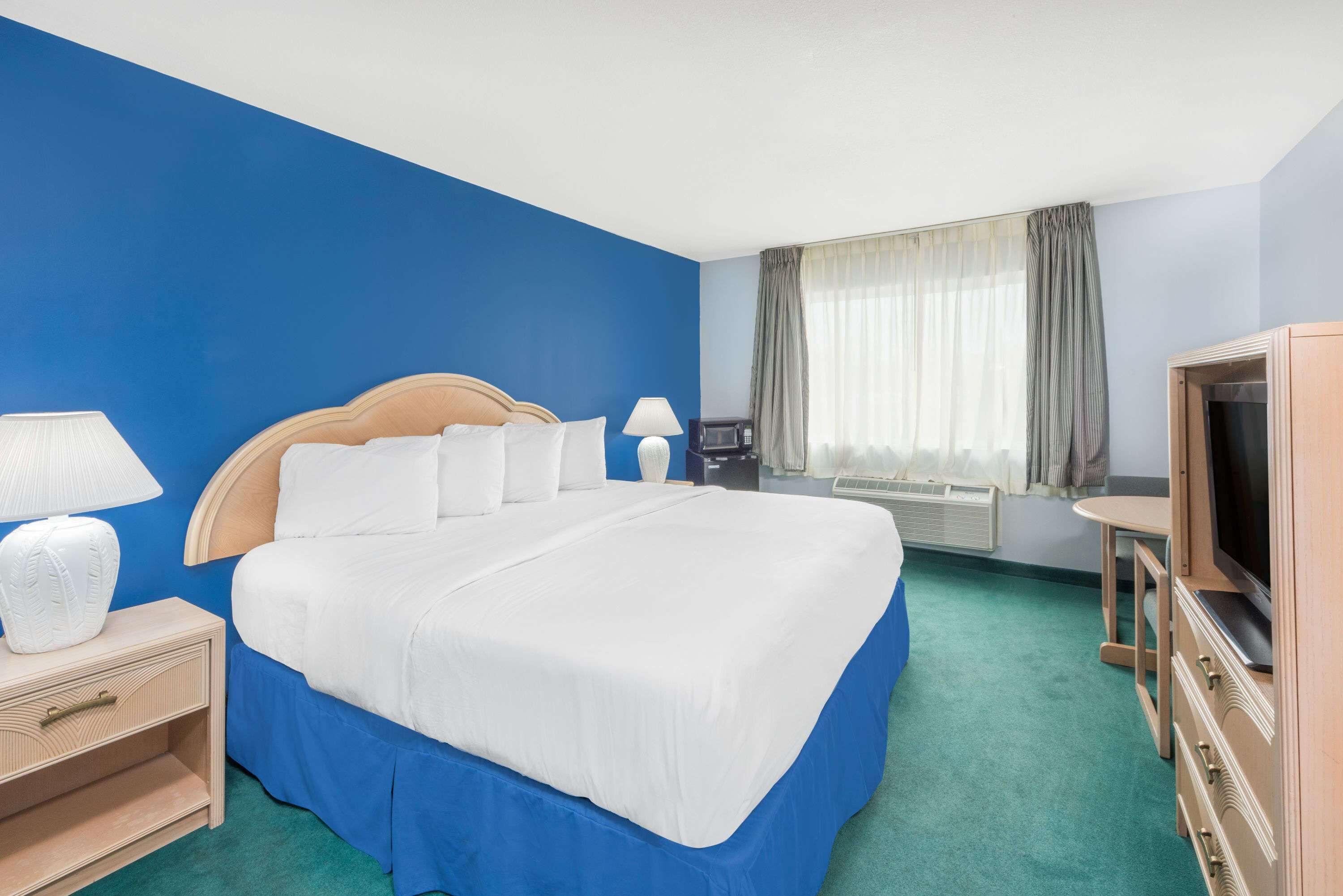 A hotel room with a large bed, bedside lamps, a television, and a window with curtains.