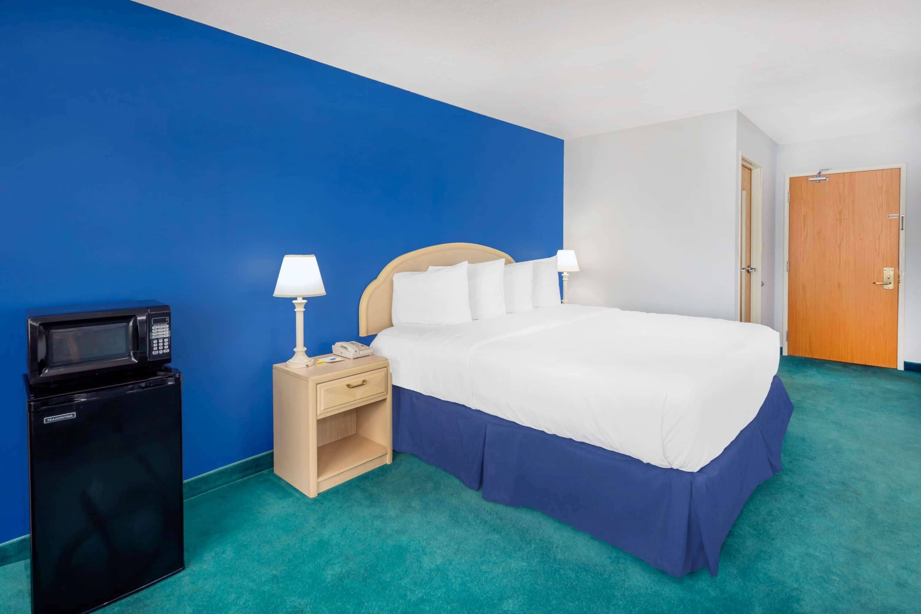 Una habitación de hotel con cama, mesita de noche, lámpara y un refrigerador negro.