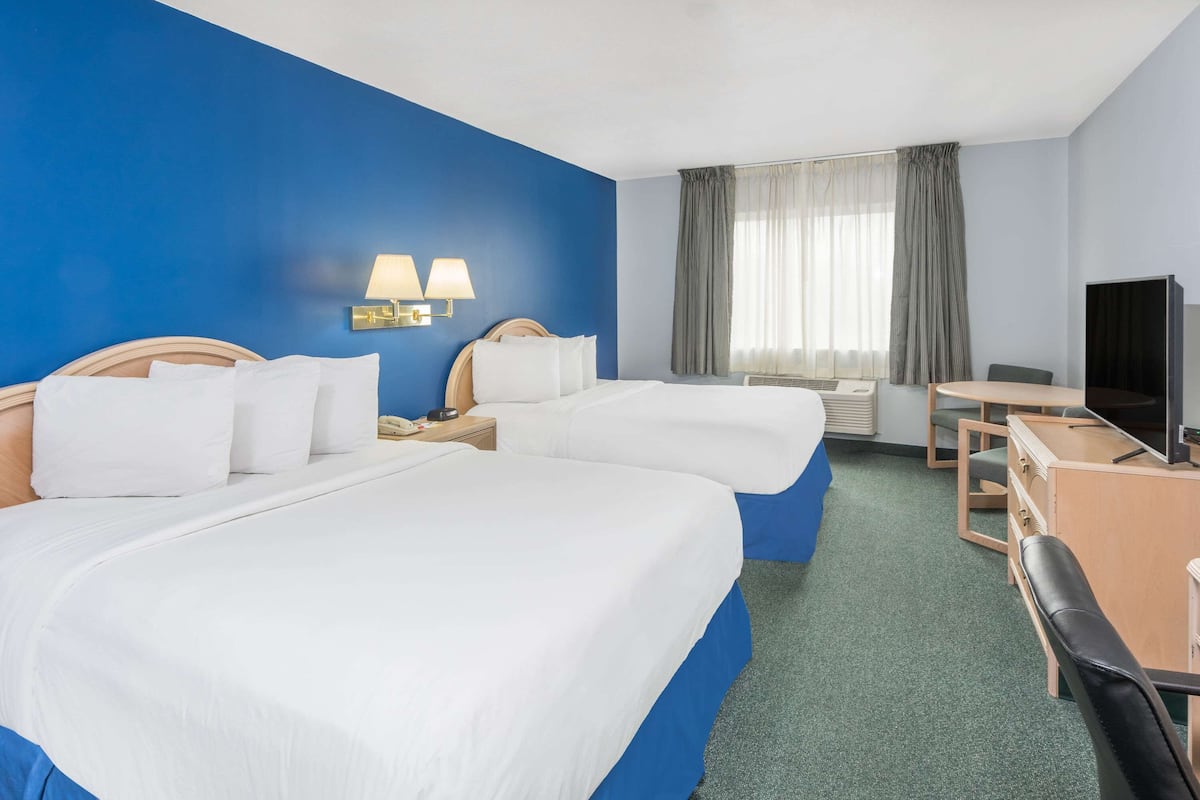 Ein Hotelzimmer mit zwei Betten, einem Schreibtisch, einem Stuhl, einem Fernseher und einem Fenster mit Vorhängen.