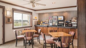 A breakfast area with wooden tables and striped chairs, a coffee machine, and a refrigerator stocked with beverages.